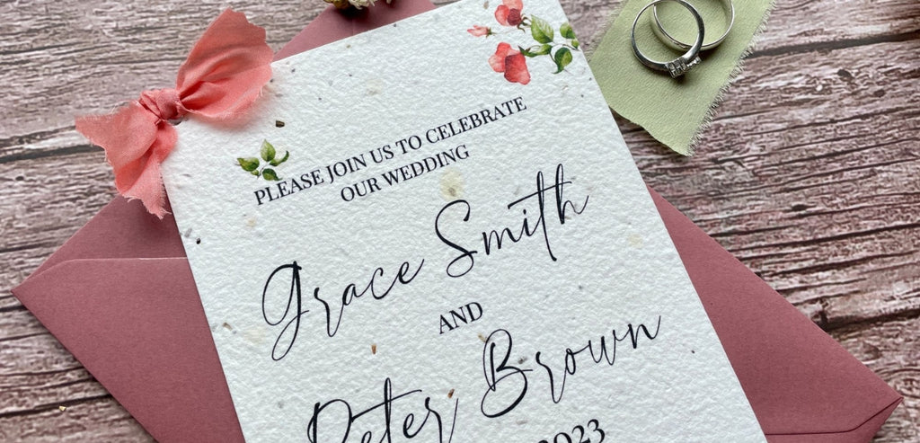 A La KArt Creations wedding invitation in the theme 'Sweet Pea', laid out on a wooden backdrop, alongside wedding rings.