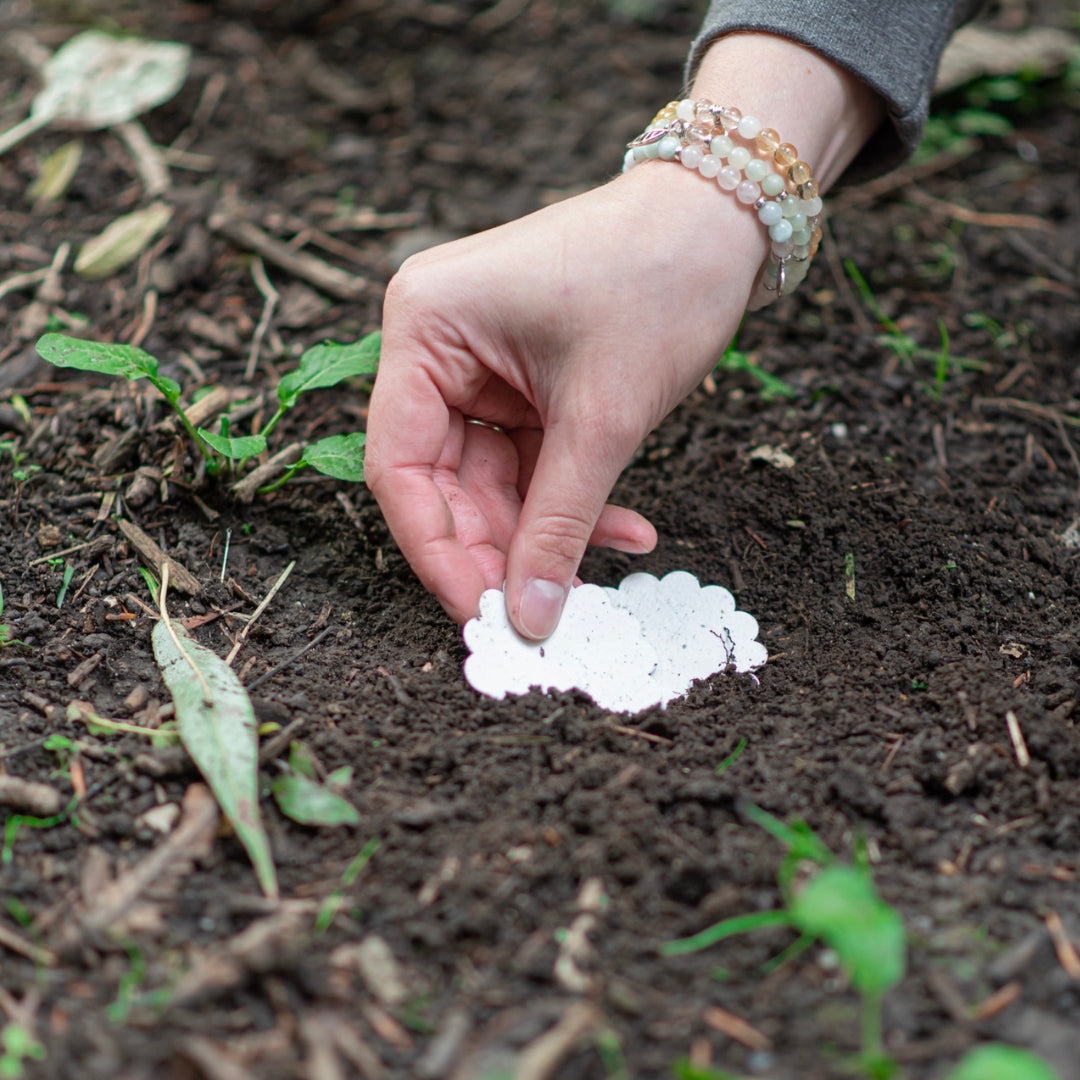 An image of Kitti, the founder of A La KArt Creations, placing a plantable product tag into the ground where it will grow into wildflowers.