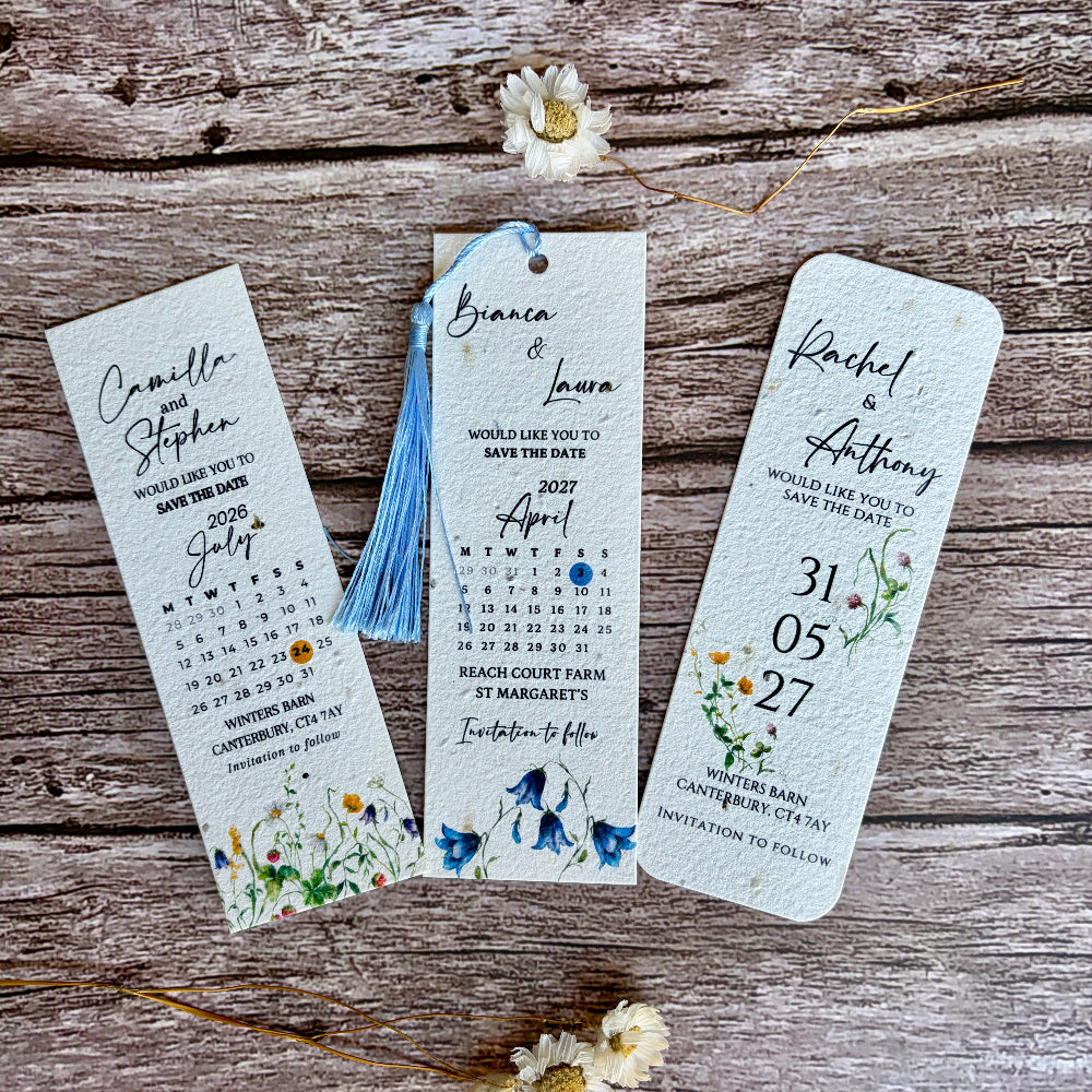 Three wedding save-the-date bookmarks with floral designs on a wooden surface.