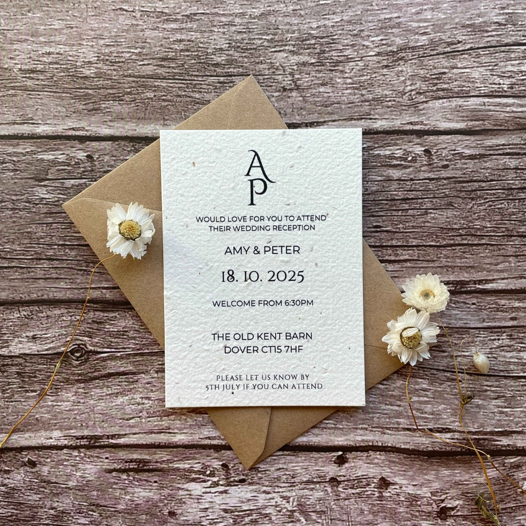 A plain seed paper evening wedding invitation card with dried flowers and a kraft paper envelope, displayed on a wooden surface.