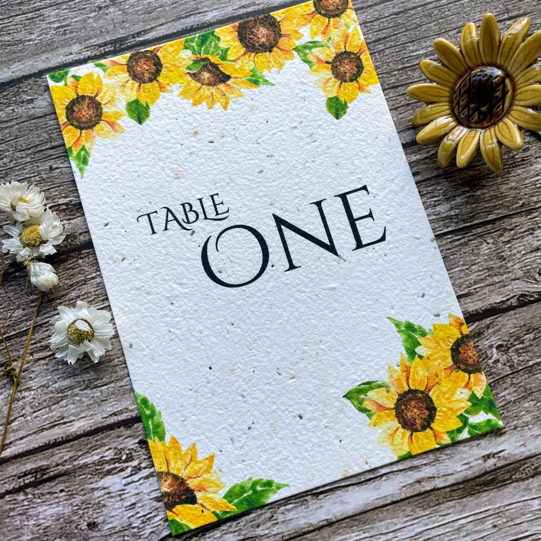 plantable seed paper wedding table number or name cards in sunflower theme, angled close-up view with floral design on wooden background, eco-friendly, alakartcreations