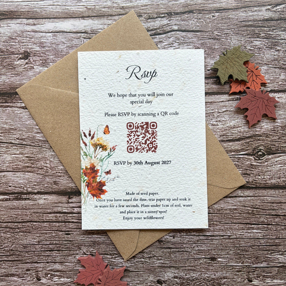 A plantable handmade paper autumn invitation card with a QR code and floral illustration, placed on top of a brown kraft envelope on a rustic wood surface with decorative autumn leaves.