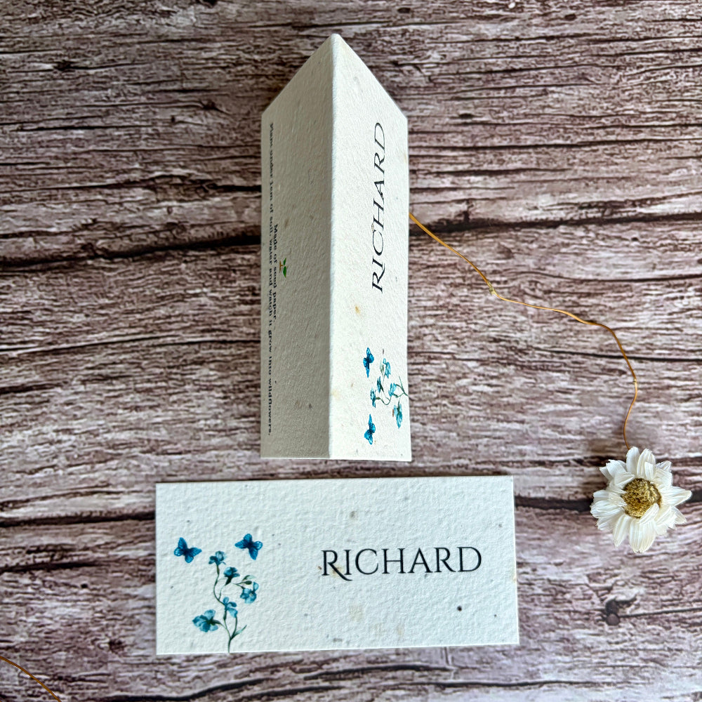 Personalised wedding plantable name card with blue sweet peas design and wooden block on a rustic wooden surface.