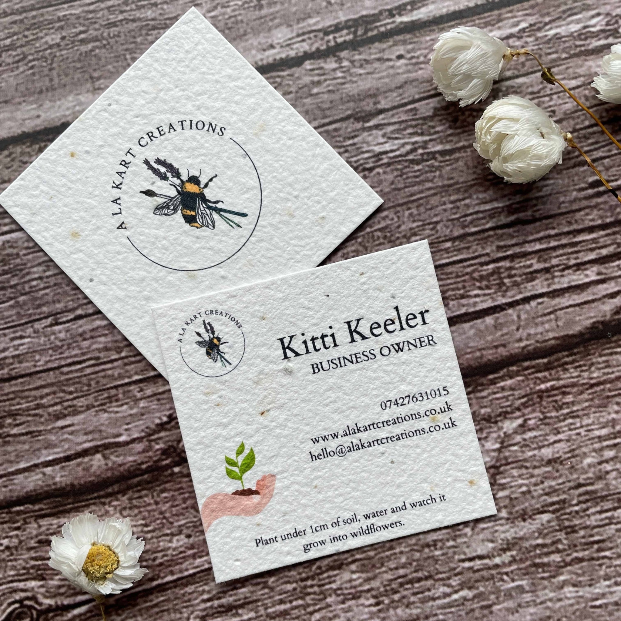 square plantable seed paper business cards with sustainable future design featuring hand holding growing seedling, angled left, alakartcreations