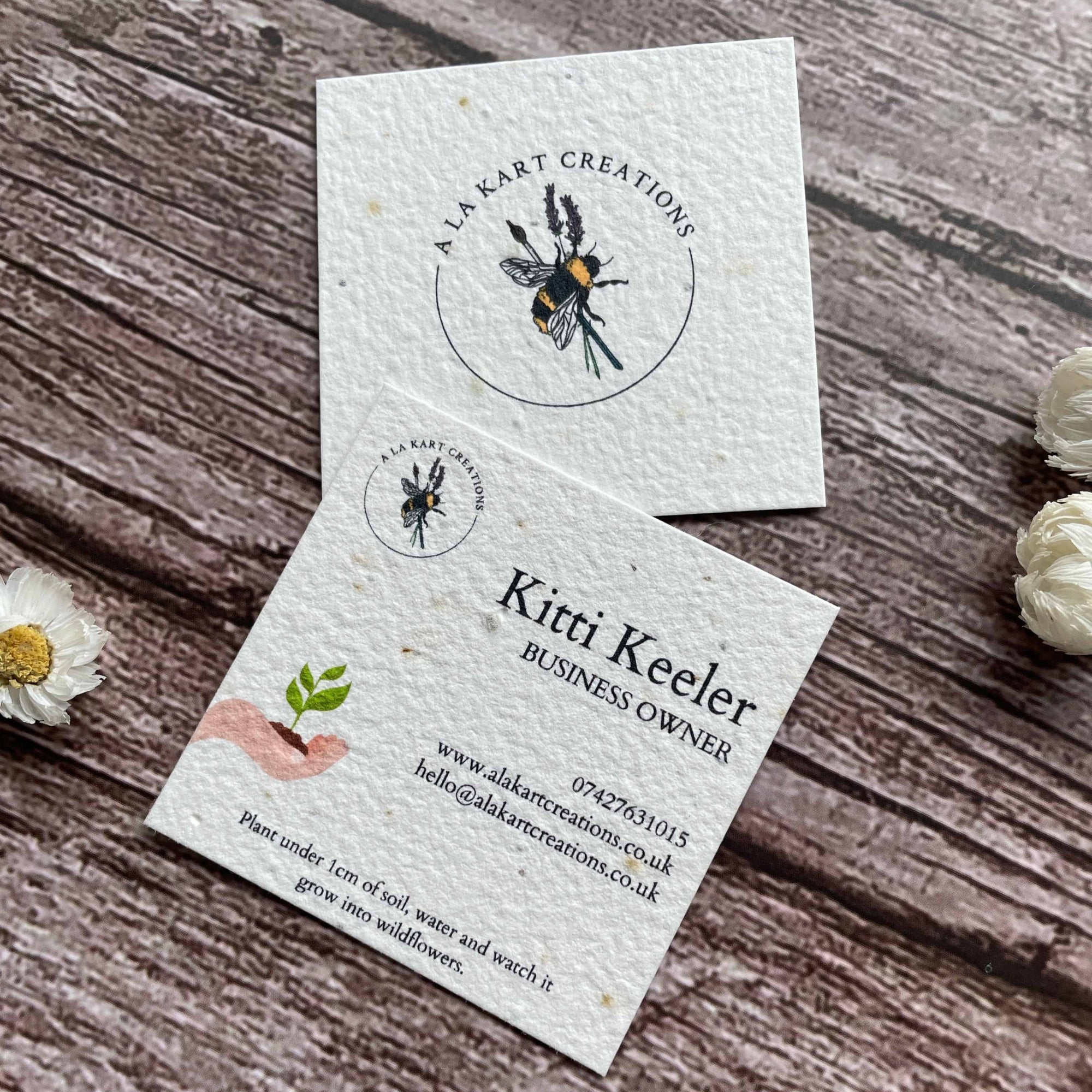 square plantable seed paper business cards with sustainable future design featuring hand holding growing seedling, angled right, alakartcreations