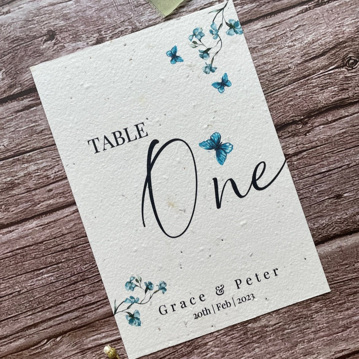 plantable seed paper wedding table number/name card with blue sweet peas, showing angled left view, floral design on wooden background