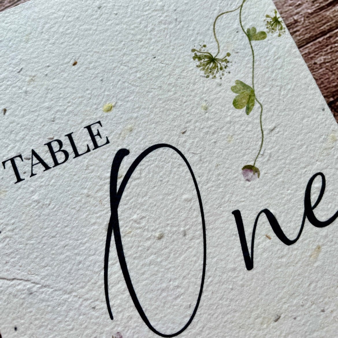 plantable seed paper wedding table number/name card with botanical design showing front close-up view, floral design on wooden background.