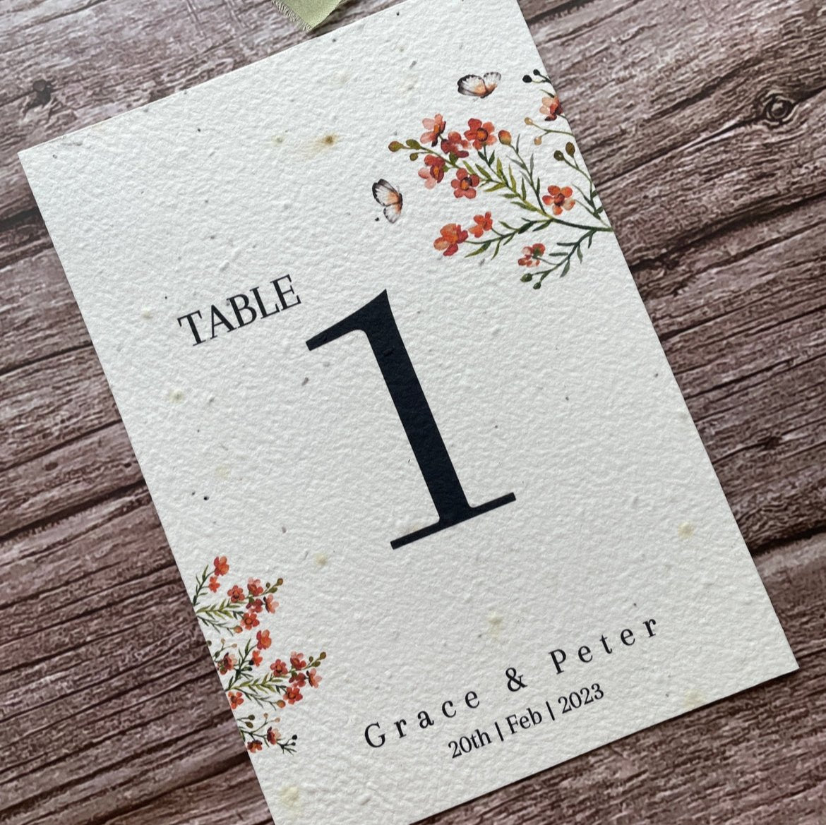 plantable seed paper wedding table number or name cards in burnt orange theme, angled left view with floral design on wooden background, eco-friendly, alakartcreations
