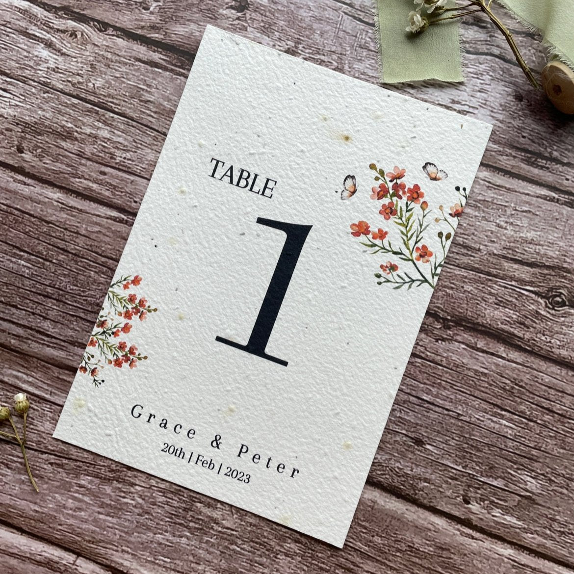 plantable seed paper wedding table number or name cards in burnt orange theme, angled view with floral design on wooden background, eco-friendly, alakartcreations