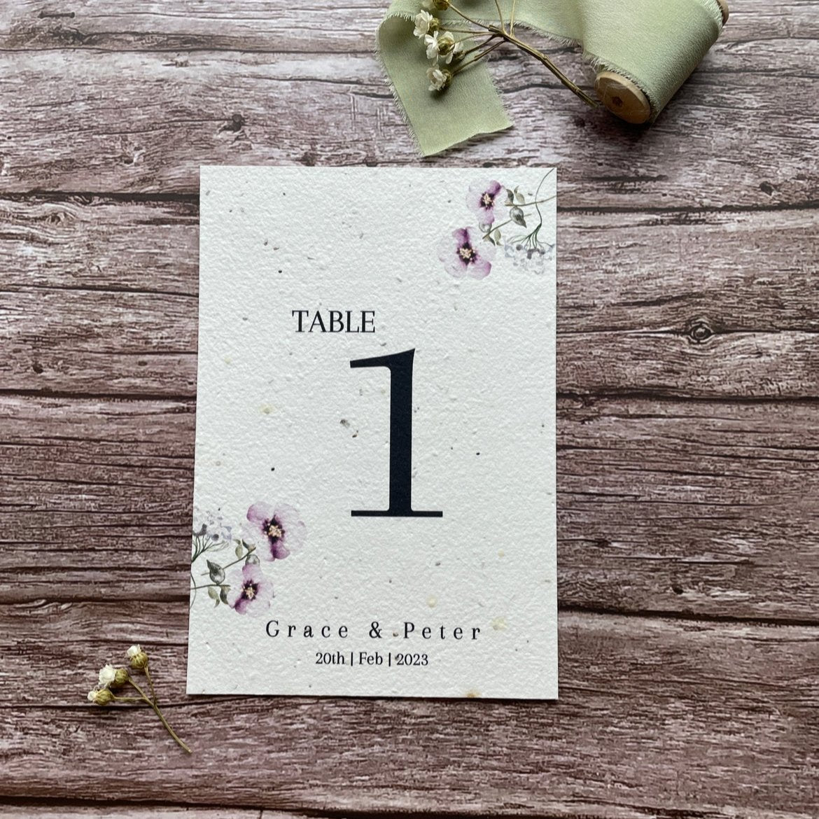 plantable seed paper wedding table number or name cards in lilac theme, front view with floral design on wooden background, eco-friendly, alakartcreations