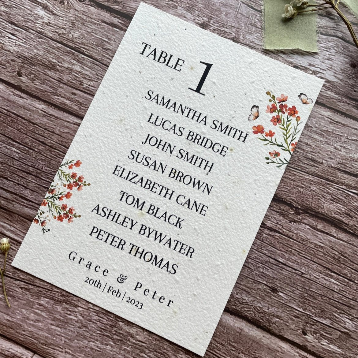 plantable seed paper wedding table seating plan in burnt orange theme, angled right view with floral design on wooden background, eco-friendly, alakartcreations