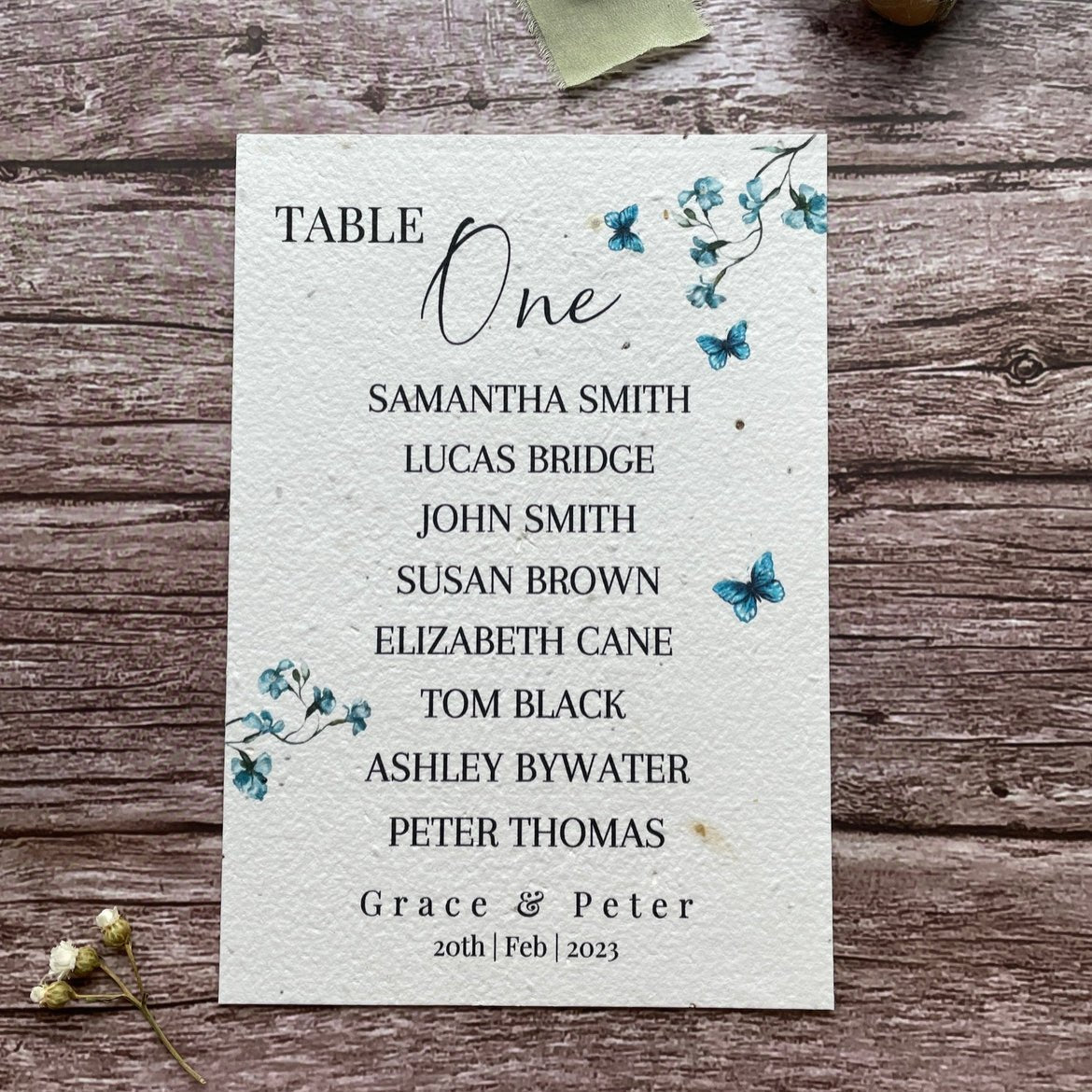 plantable seed paper wedding table seating plan in dusty blue theme, front view with floral design on wooden background, eco-friendly, alakartcreations