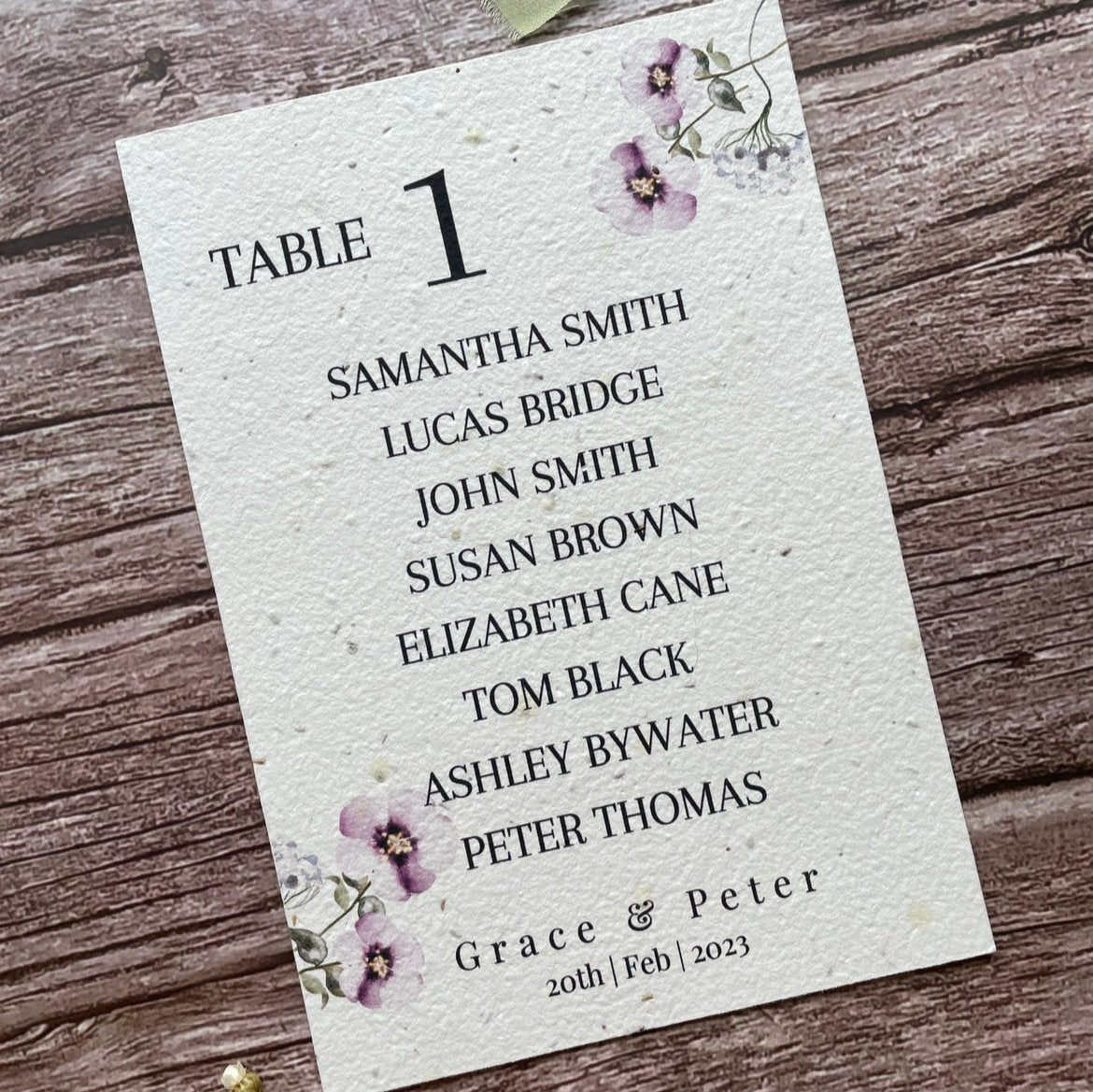 plantable seed paper wedding table seating plan in lilac theme, angled left view with floral design on wooden background, eco-friendly, alakartcreations