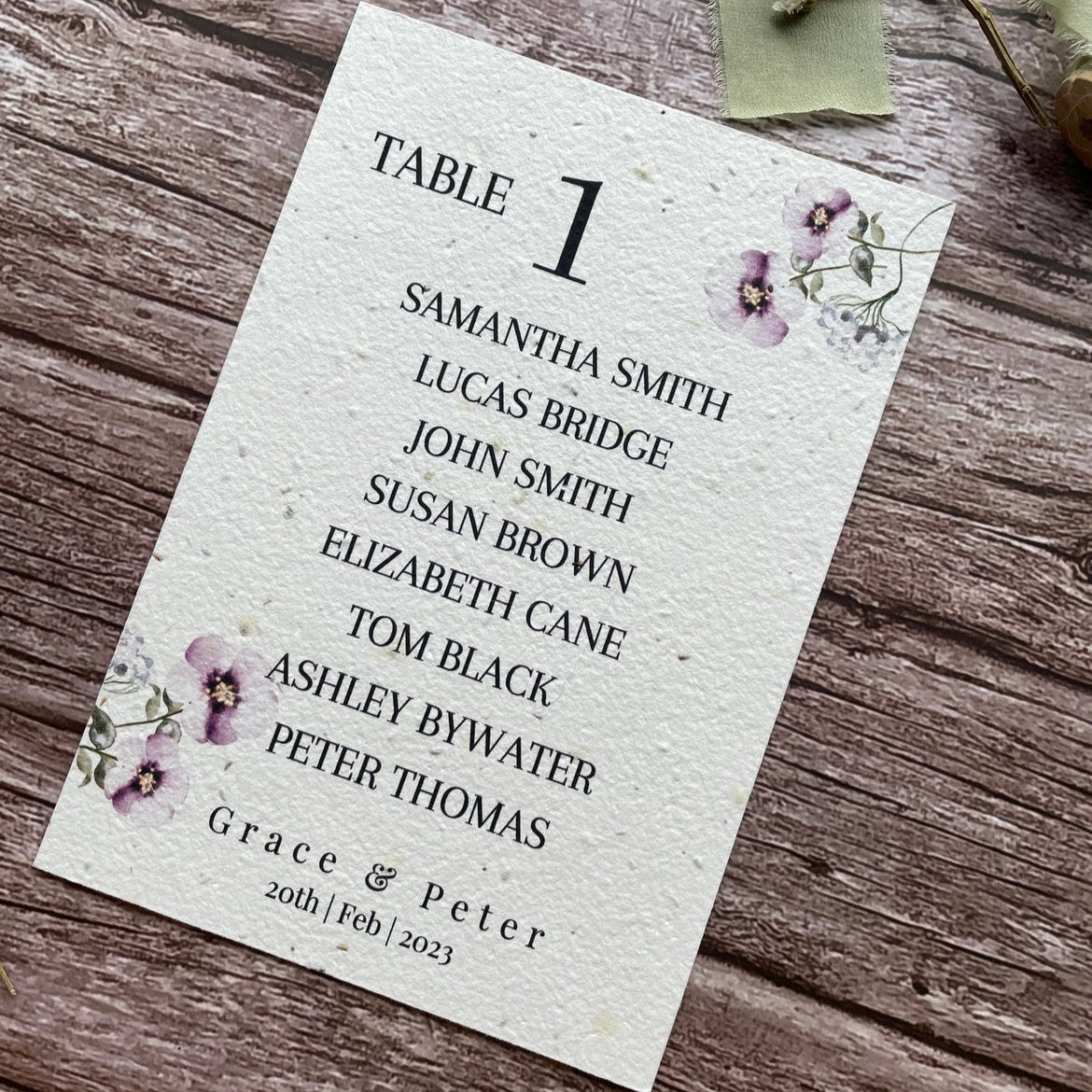 plantable seed paper wedding table seating plan in lilac theme, angled right view with floral design on wooden background, eco-friendly, alakartcreations