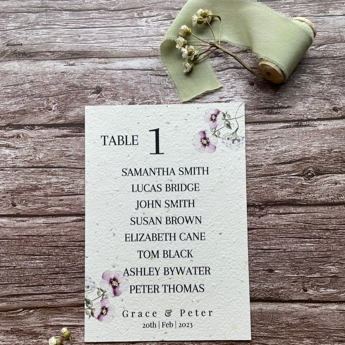 plantable seed paper wedding table seating plan in lilac theme, front view with floral design on wooden background, eco-friendly, alakartcreations