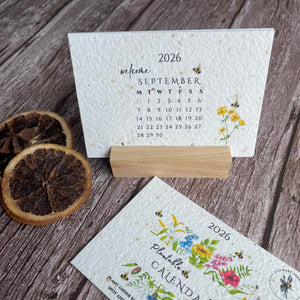 Two seed paper calendars with floral designs in a wooden stand.