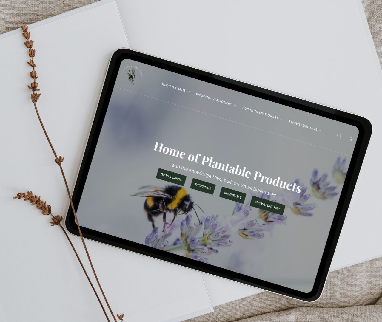 A La KArt Creations home page displayed on an ipad, laid on a desk alongside dried flowers.