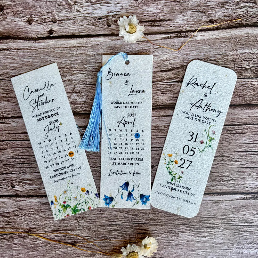 Three wedding seed paper save the date bookmarks with floral designs on a wooden surface.