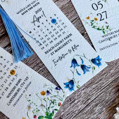 Plantable save the date bookmarks with floral designs and tassels on a wooden surface