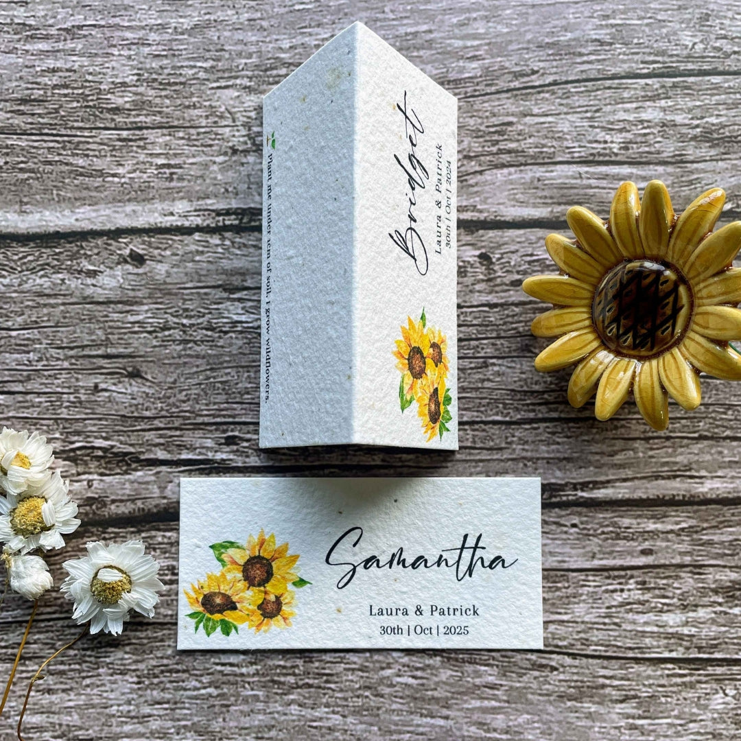 plantable seed paper wedding guest place cards sunflower theme, flat and standing views one above other on wooden background with sunflower.