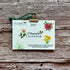 A 2027 plantable paper calendar card by A La KArt Creations featuring watercolor floral illustrations and a green hanging ribbon, displayed on a rustic weathered wood background.