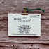 A 2027 plantable paper calendar card by La Kart Creations, clipped with a gold metal clip and green string, displayed on a rustic brown wood background.