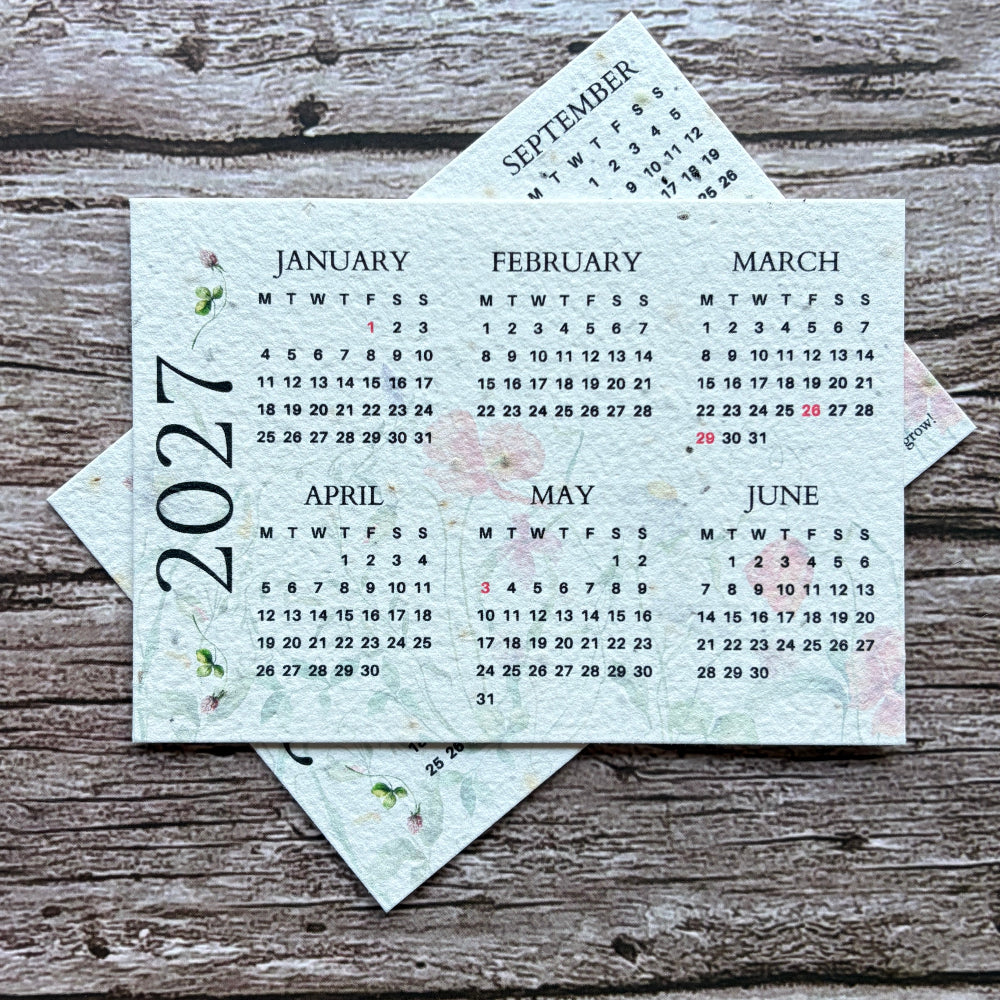 A set of six months printed plantable calendar pages for 2027, arranged in a star shape on a rustic, weathered gray wood background.