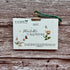 A 2027 Plantable Calendar by A La Kart Creations, made from textured watercolor paper with floral illustrations and a green hanging string, clipped to a rustic wood background.