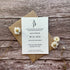 A plain seed paper evening wedding invitation card with dried flowers and a kraft paper envelope, displayed on a wooden surface.