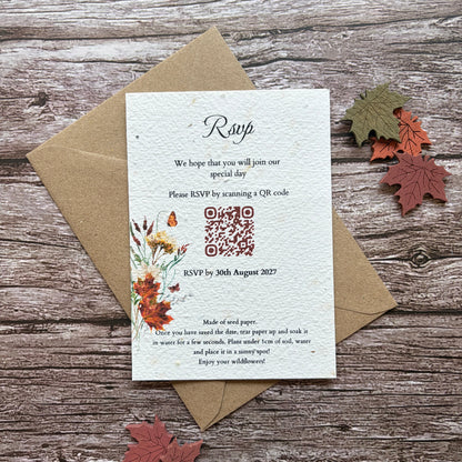 A handmade seed paper evening invitation card with a QR code and floral illustration, placed on top of a brown kraft envelope on a rustic wood surface with decorative autumn leaves.