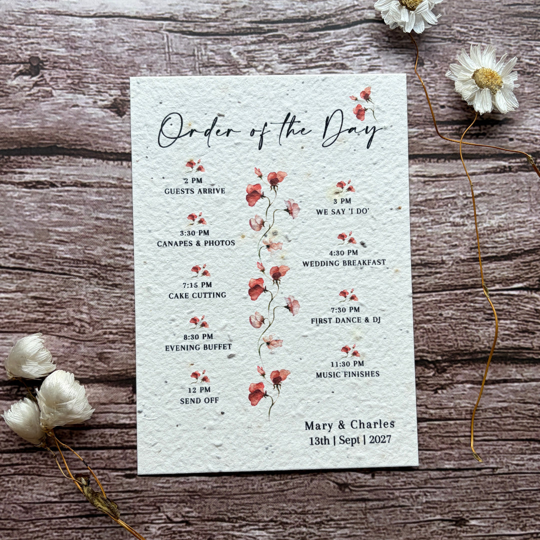 Wedding seed paper order of service with pink sweet peas on a wooden surface with flowers