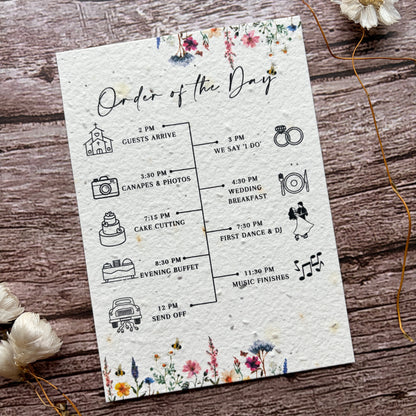 Wedding order of the day card on a wooden surface with flowers.