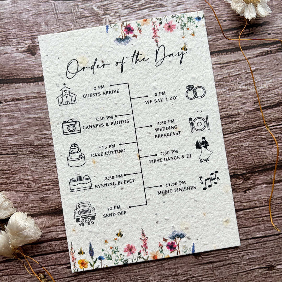 Wedding order of the day card on a wooden surface with flowers.