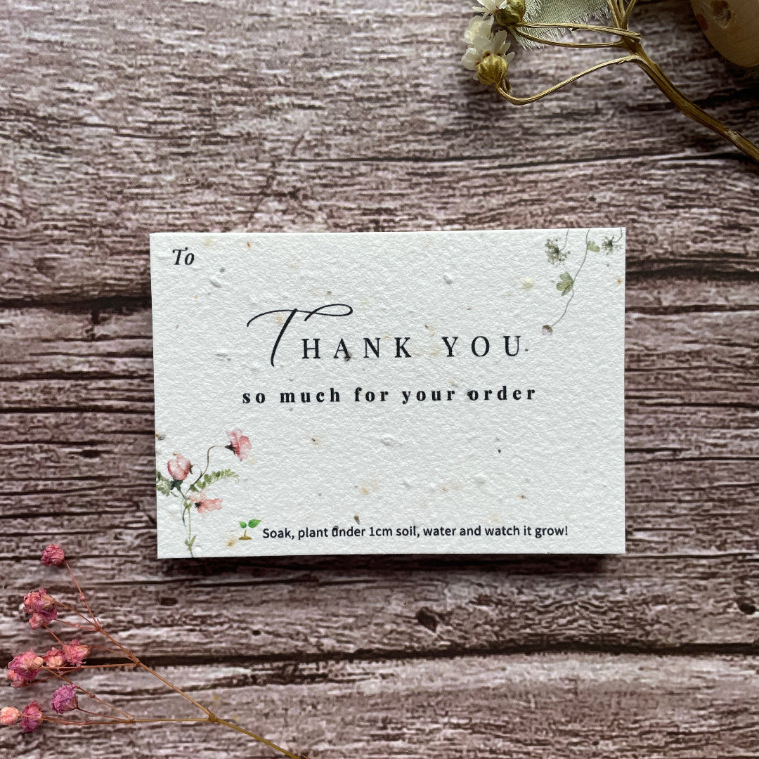 Seed paper thank you card with 'Thank you for your order' message on a wooden surface with flowers.