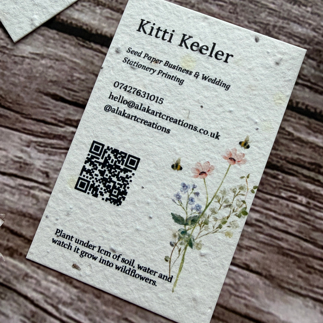 Plantable seed paper business card with floral design and QR code on a wooden surface