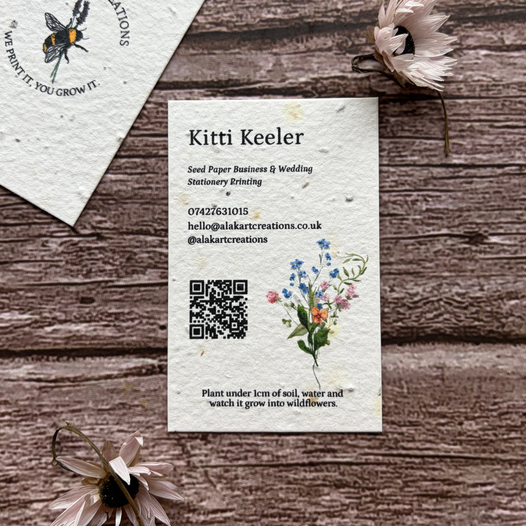 Two seed paper business cards on a wooden surface with floral designs and text.