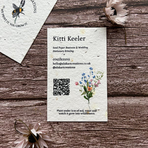 Two seed paper business cards on a wooden surface with floral designs and text.