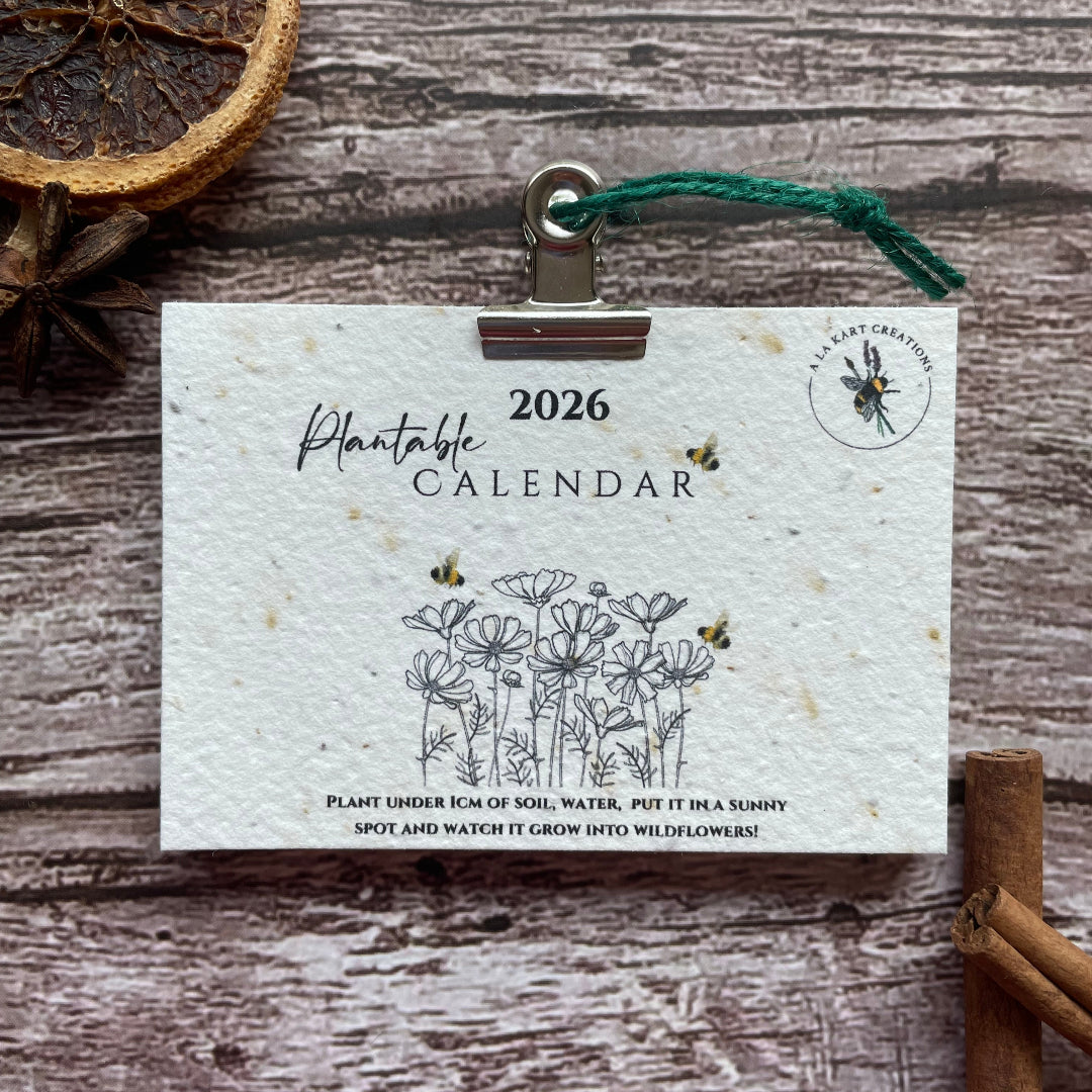 2026 calendar card with nature-themed design on a wooden surface with cinnamon sticks and dried oranges.