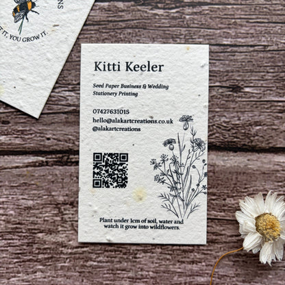 Seed paper business card with QR code on a wooden surface with a cornflower.