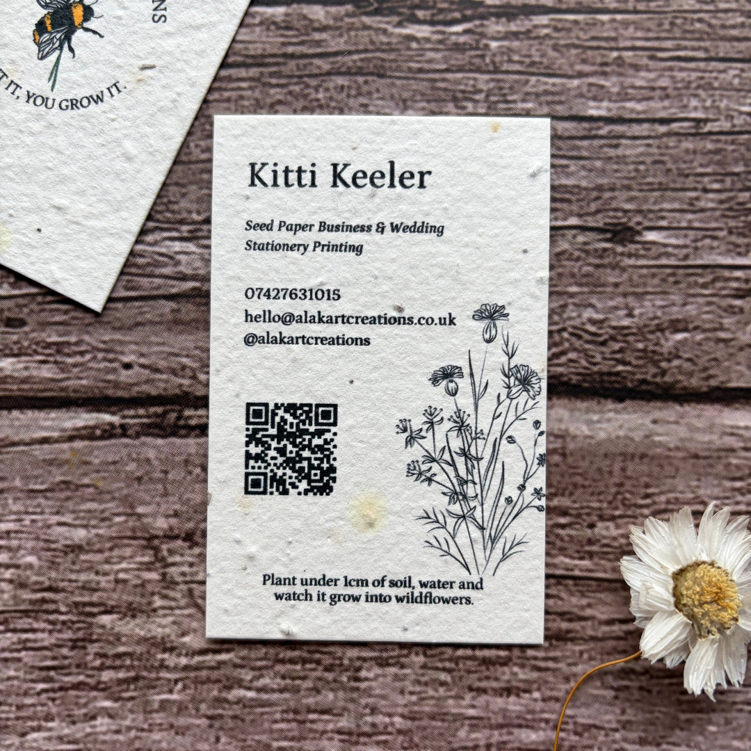 Seed paper business card with QR code on a wooden surface with a cornflower.