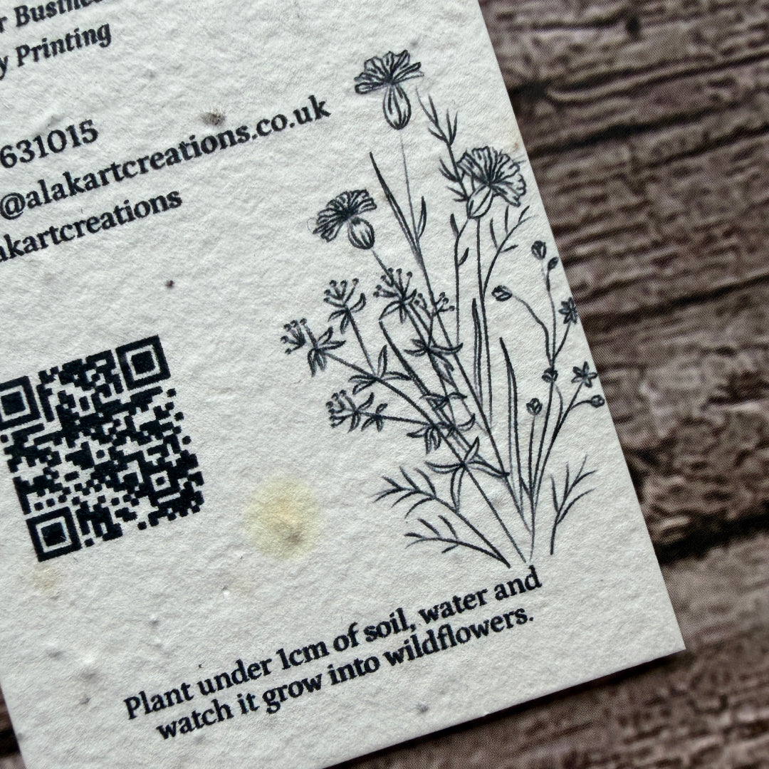 Seed paper business card with QR code and cornflower design on a wooden surface
