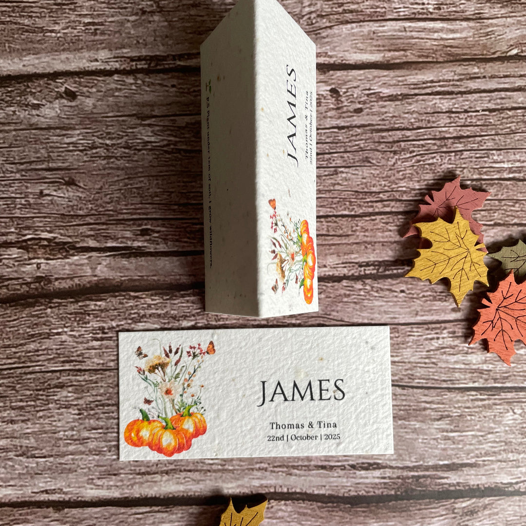 Wedding guest card with 'JAMES' branding on a wooden surface with autumn flowers and pumpkins.