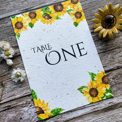 plantable seed paper wedding table number or name cards in sunflower theme, angled close-up view with floral design on wooden background, eco-friendly, alakartcreations