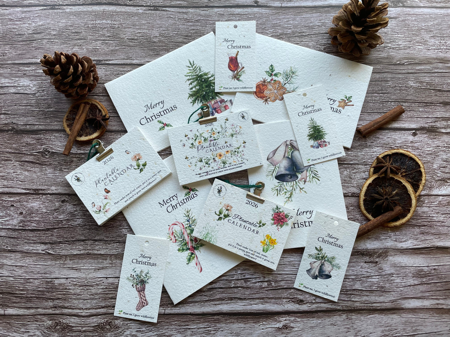 Collection of plantable seed paper Christmas-themed greeting cards 2026 calendars and tags on a wooden surface with decorative elements.