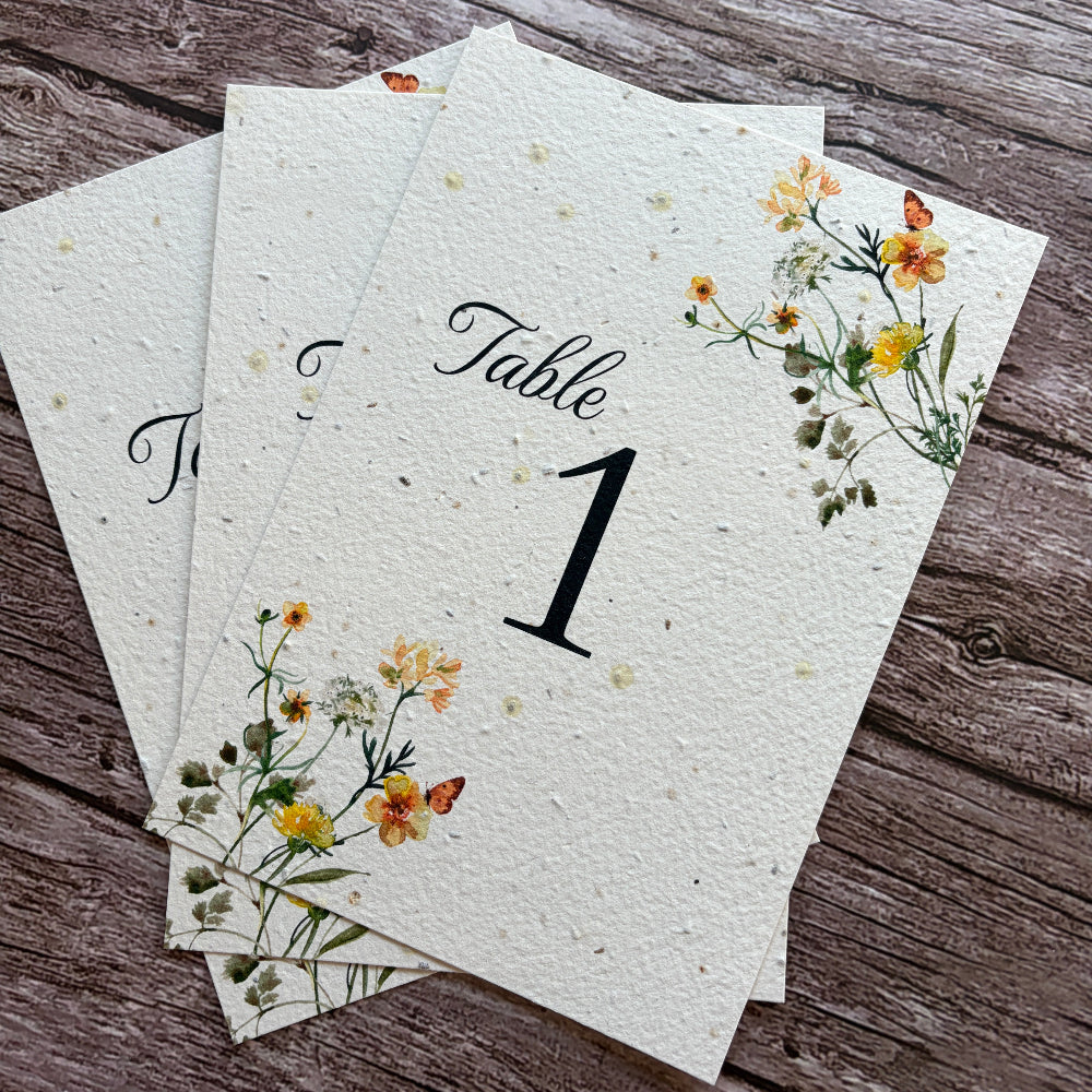 Plantable table number cards for weddings with floral designs on a wooden surface