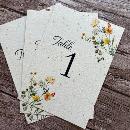 Plantable table number cards for weddings with floral designs on a wooden surface