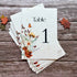 Plantable table number card with floral design on a wooden surface