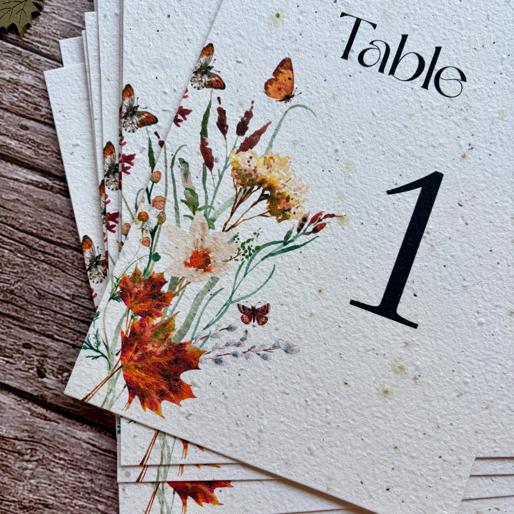 Stack of plantable table number cards with autumn leaves design on a wooden surface