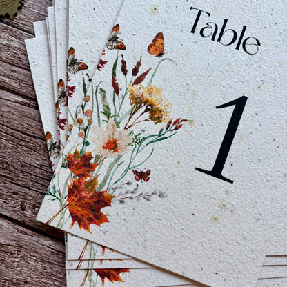 Stack of plantable table number cards with autumn leaves design on a wooden surface