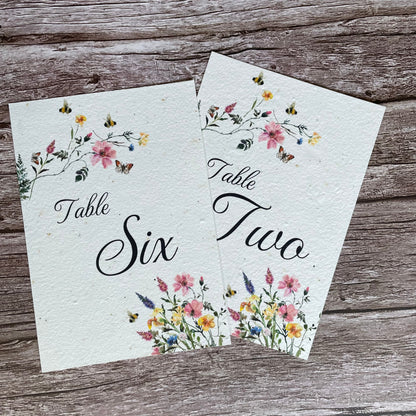 Two floral table number cards on a wooden surface made of seed paper